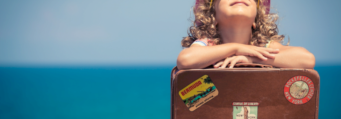 Kind sitzt mit Koffer am Strand