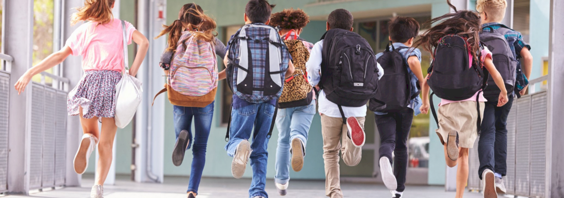 Schulkinder laufen gemeinsam mit ihren Schulranzen auf den Rücken auf eine Schule zu.